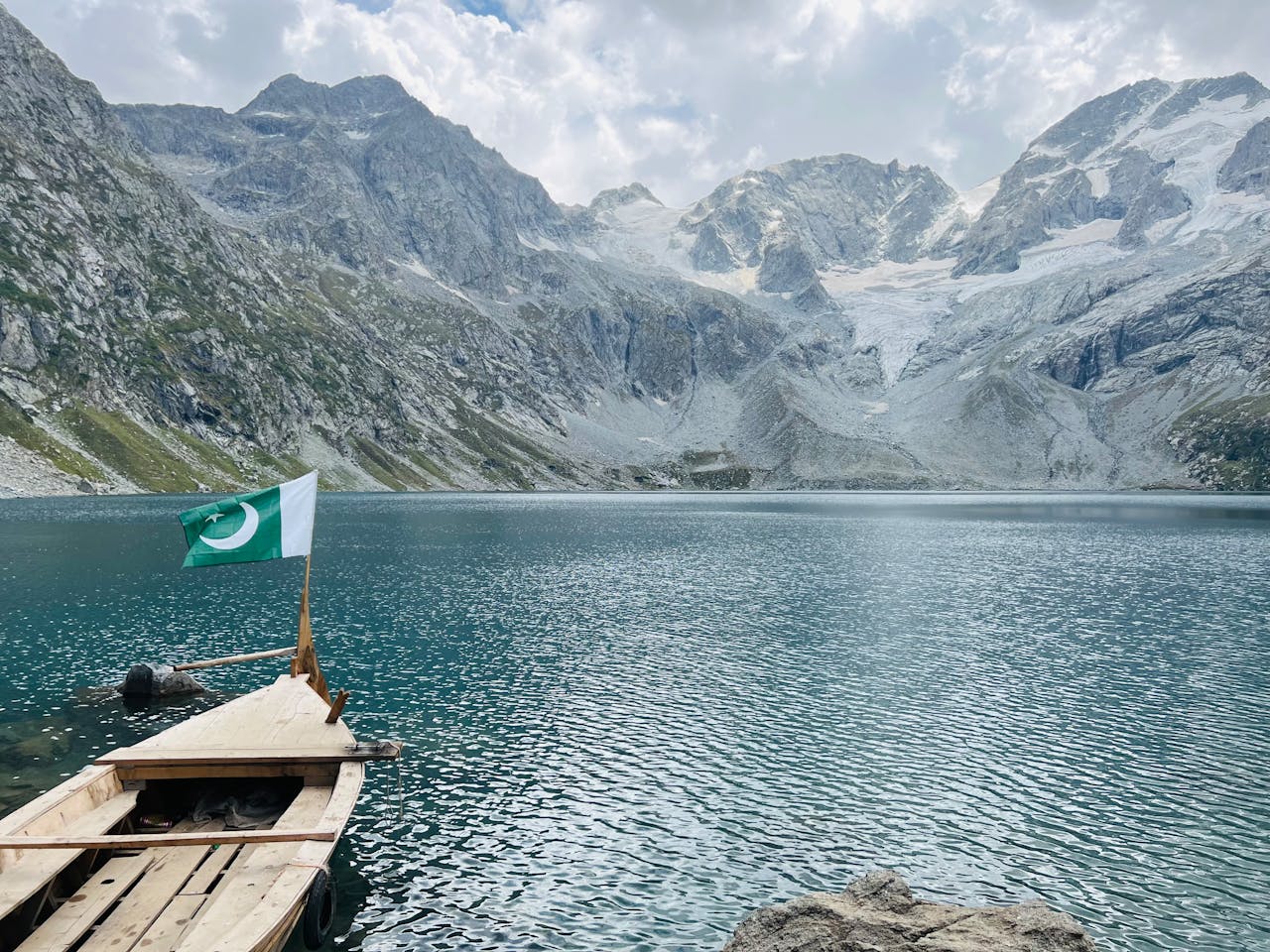 A serene lake with mountains and a Pakistani flag on a boat, capturing peaceful natural beauty.